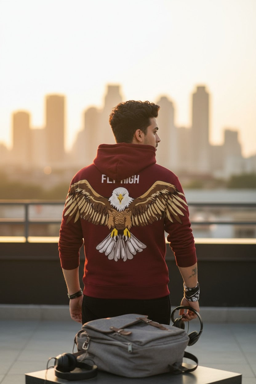 Man wearing a red hoodie with an eagle design, standing on a rooftop with a city skyline in the background.