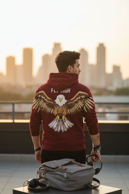 Man wearing a red hoodie with an eagle design, standing on a rooftop with a city skyline in the background.