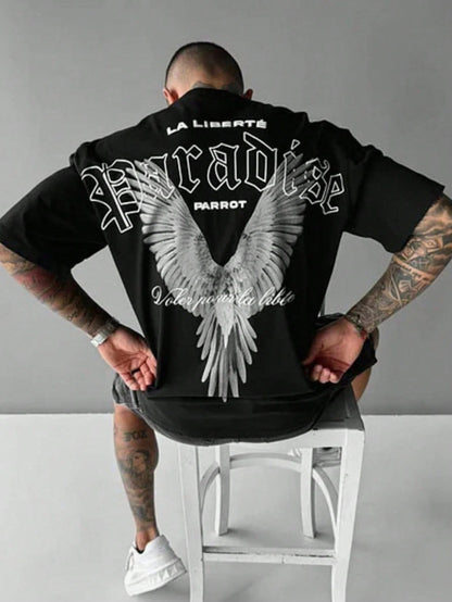 Person wearing a black hoodie with white text and angel wings design on the back, sitting on a white stool against a gray background.