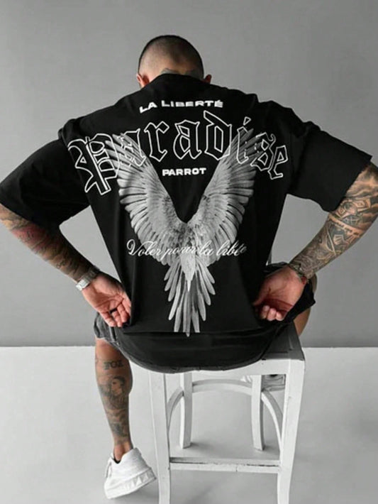 Person wearing a black hoodie with white text and angel wings design on the back, sitting on a white stool against a gray background.