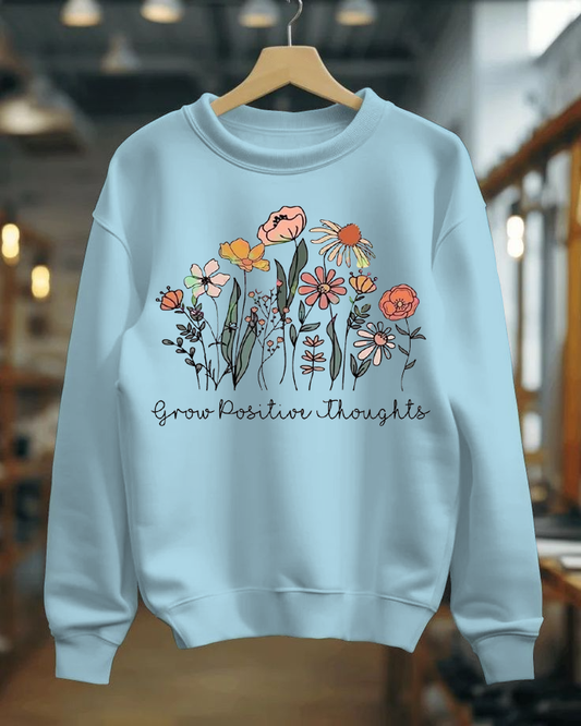 Light blue sweatshirt with floral design and 'Grow Positive Thoughts' text on a hanger.